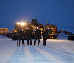 Expeditioners standing in the lights of plant equipment on runway at twilight