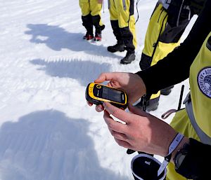 An expeditioner holds a small yellow GPS device.