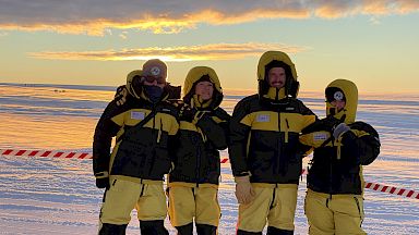 4 expeditioners stand together on the ice.