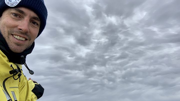 An Antarctic expeditioner taking a selfie in front of a group of penguins