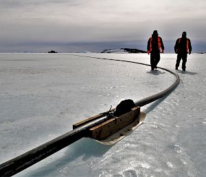 Two expeditioners walk alongside a fuel line