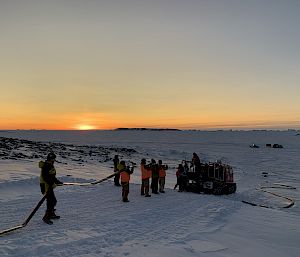A group of expeditioners help to unroll a fuel line behind a vehicle