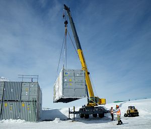 Crane lifting a silver container onto a stack of similar containers.