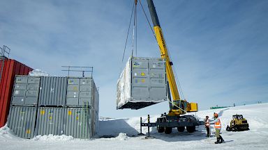 Crane lifting a silver container onto a stack of similar containers.