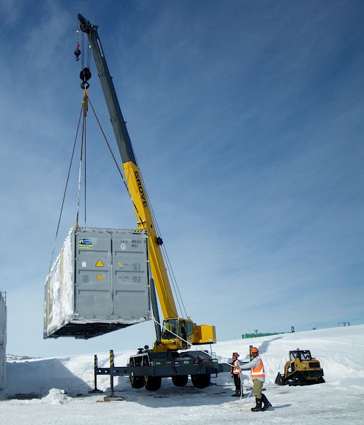 Crane lifting a silver container onto a stack of similar containers.