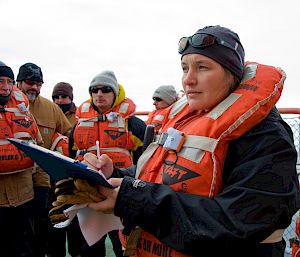 Deputy Voyage Leader marking on clipboard surrounded by expeditioners on the deck of ship