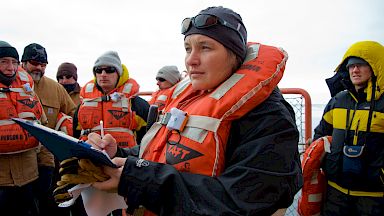 Deputy Voyage Leader marking on clipboard surrounded by expeditioners on the deck of ship
