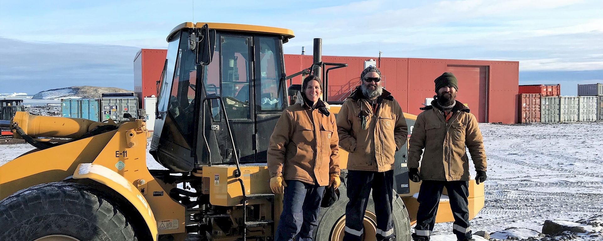 Three expeditioners stand in front of yellow tractor vehicle
