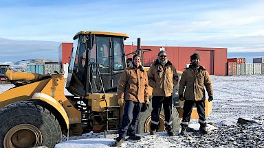 Three expeditioners stand in front of yellow tractor vehicle