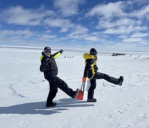 Two expeditioners walking across the snowy camp site