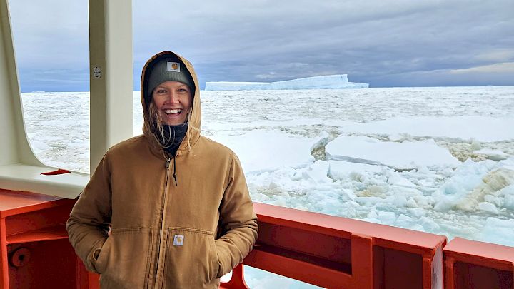 Expeditioner on RSV Nuyina with the pack ice in the background and a large tabular iceberg on the horizon