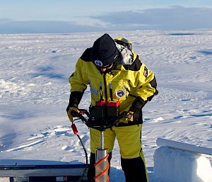 Expeditioner in Antarctic clothing using the ice core drill