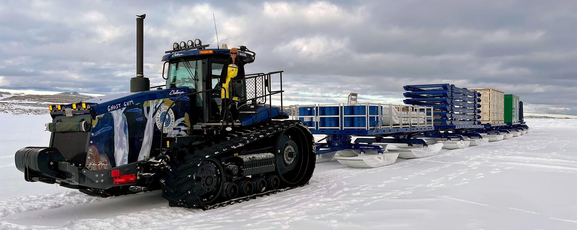 A tractor tows a train of containers on sleds across the ice.