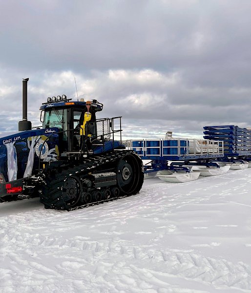 A tractor tows a train of containers on sleds across the ice.