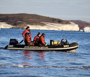 An inflatable boat motors across the still, blue water. There is an icy coastline in the distance.