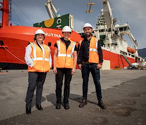 3 people stand on the wharf with RSV Nuyina in the background