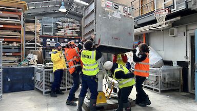 Expeditioners lift a metal crate and check below it.