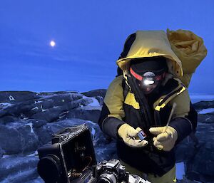 An expeditioner holding a piece of scientific equipment in the dark in Antarctica