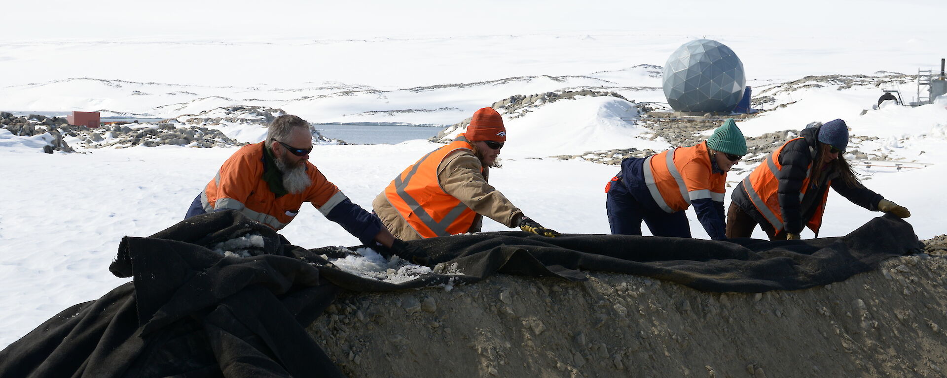 Expeditioners move a large, black sheet on the ground.