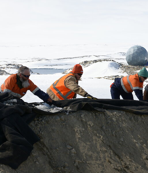 Expeditioners move a large, black sheet on the ground.