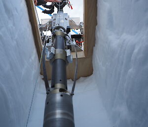 An expeditioner lowers a drill into a trench cut out of the snow.